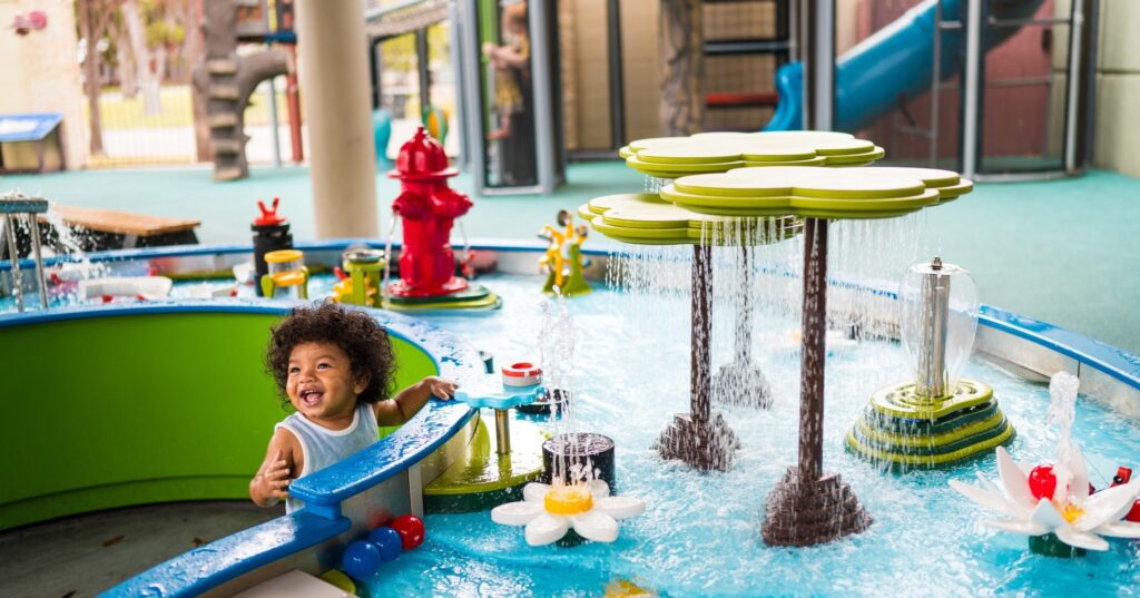 A child laughing at a colorful indoor water play table