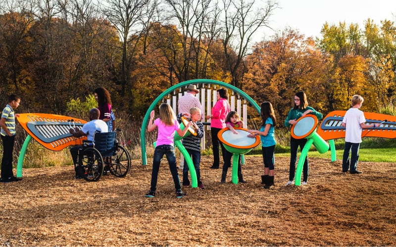 Children playing outdoor musical sculptures on a woodchip playground